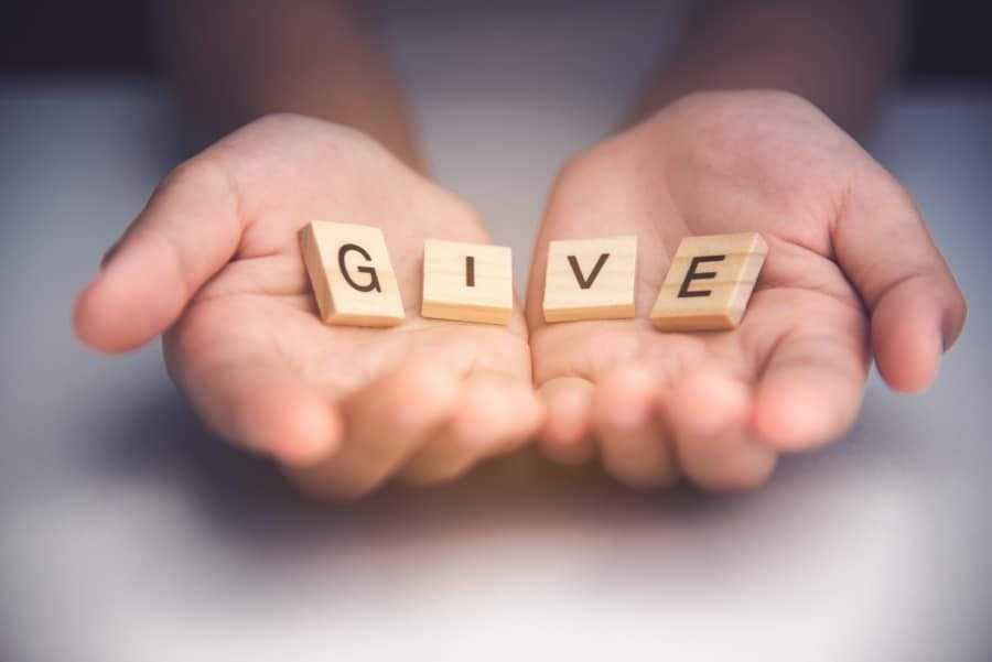 GIVE written in small wood tiles held in two outstretched hands