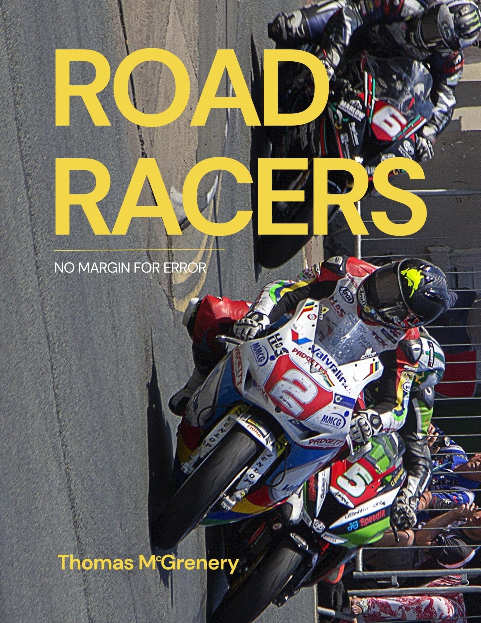 Three motorbike riders enter Parliament Square on the Isle of Man during a TT race. The image is rotated 90 degrees such that the motorbikes appear to be adhering to a vertical wall of asphalt.