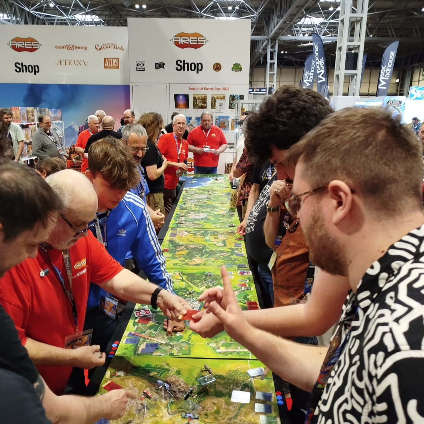 Long line of people playing a modified board game for competition. Green boards on a black table.