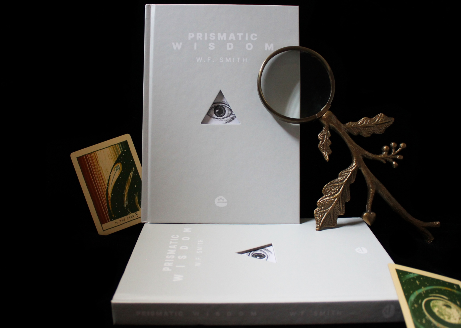 White book titled PRISMATIC WISDOM, with triangular hole in the center showing an eye