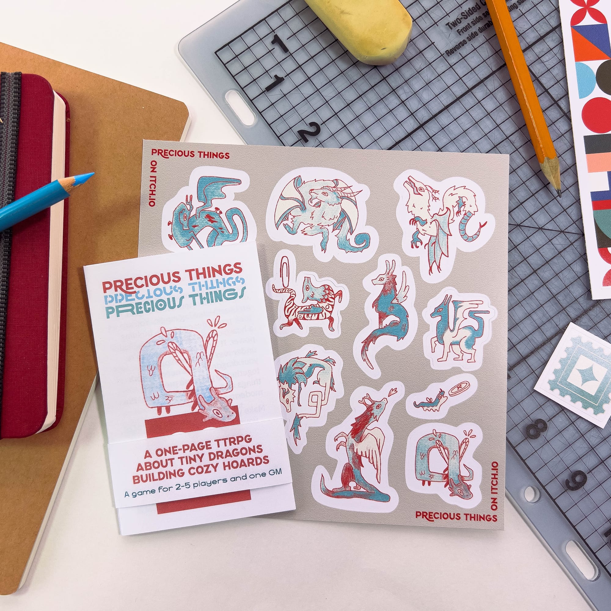 A Photo of the small zine next to the Precious Things sticker sheet with 12 dragon illustrations. 