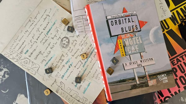 The Orbital Rules rulebook on top of a pile of records, with metal dice and a notebook nearby.