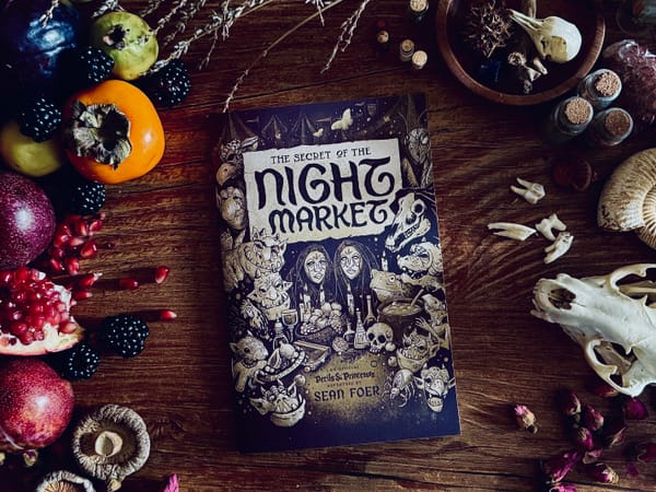 An photo of the front cover of The Secret of the Night Market surrounded by fruits, herbs and bones.