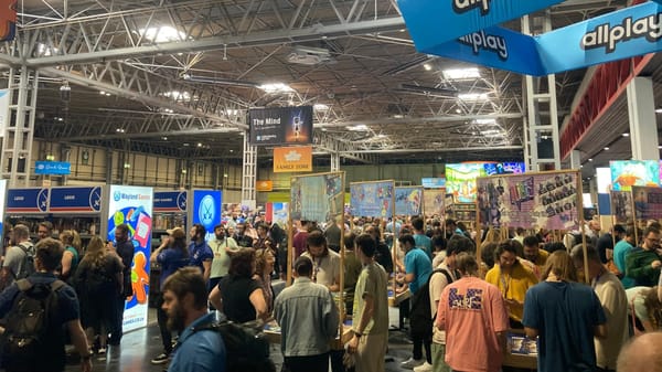 Crowd of UKGE attendees inside the convention center. A blue sign hanging above reads "allplay"