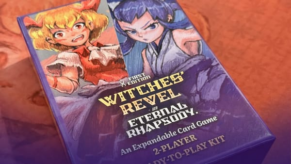 A photo of the Witches' Revel 2-Player Ready-to-Play Kit, a board game box with a joyful red-dressed witch and a dour blue-dressed witch facing off against each other.