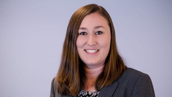 Headshot of Melinda Prickett in a dark grey suit jacket, smiling against a light grey background.